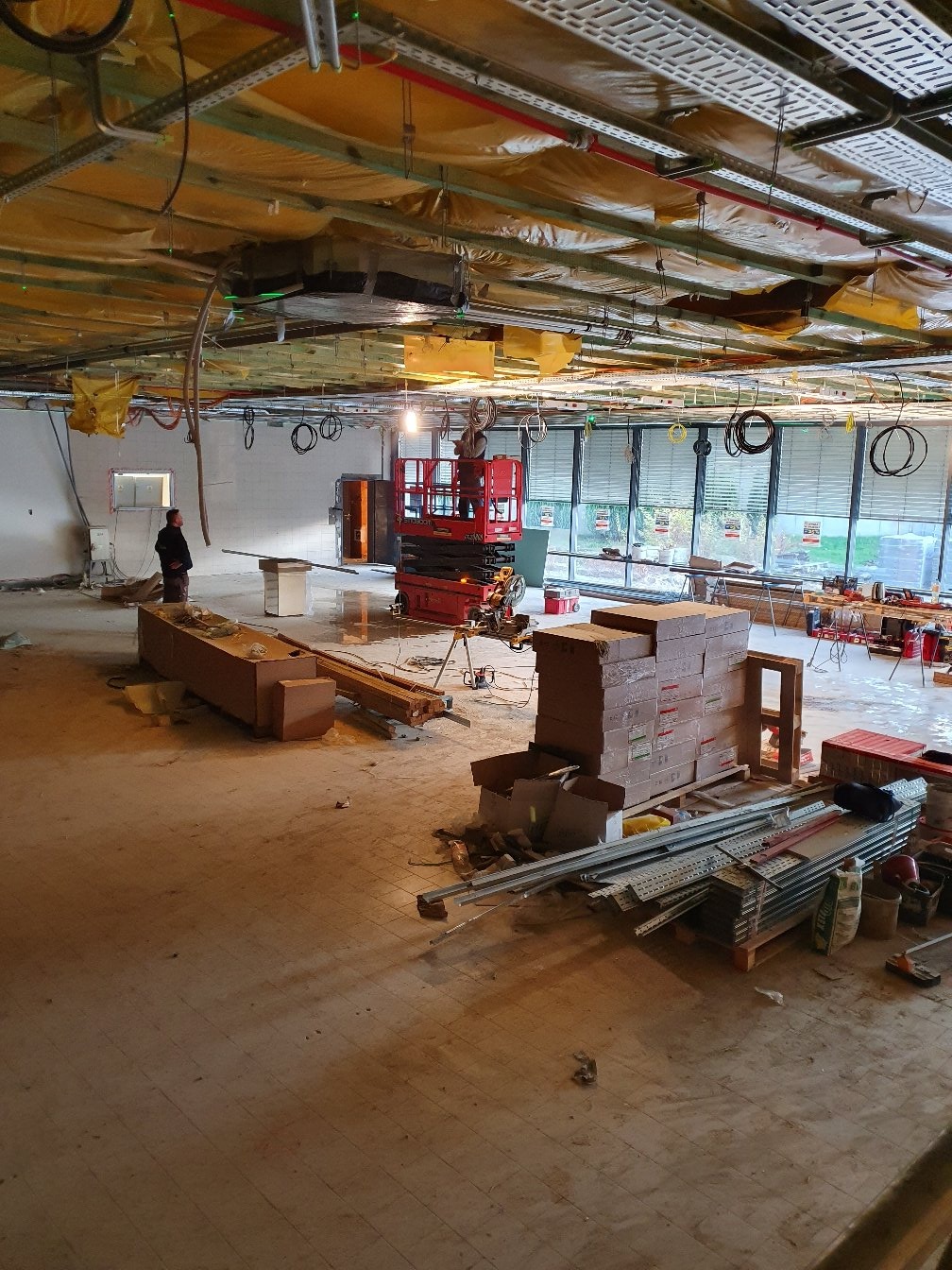 Wnętrze biura w Gdańsku w trakcie remontu, widoczna podwieszana konstrukcja sufitu, instalacje, podnośnik i materiały budowlane.