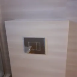 Przycisk spłuczki podtynkowy, chromowany, zamontowany na ścianie wykończonej płytkami imitującymi drewno w odcieniach beżu.