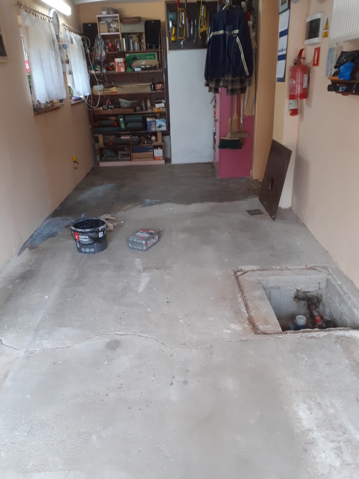 Przygotowane do remontu pomieszczenie gospodarcze z odsłoniętym włazem do instalacji, widoczne wiadro z gruntem Optiva Primer i akcesoria malarskie.