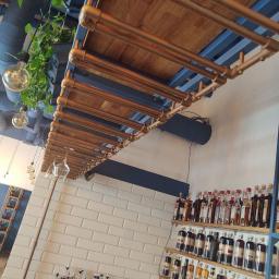 Nla Digital Group sp. z o.o. - Industrialny wystrój baru: półki z drewnianymi blatami i miedzianymi rurami podwieszone pod sufitem, białe płytki metra na ścianie, butelki alkoholu na półkach, wiszące żarówki i rośliny.