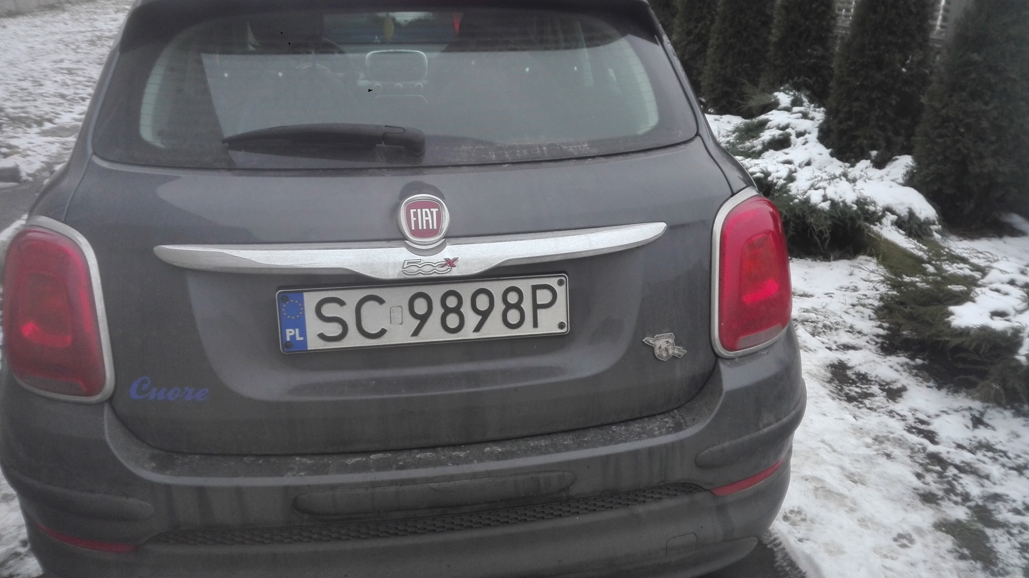 Tył szarego samochodu Fiat 500X z polską tablicą rejestracyjną SC 9898P, zaparkowanego na śniegu obok iglaków.