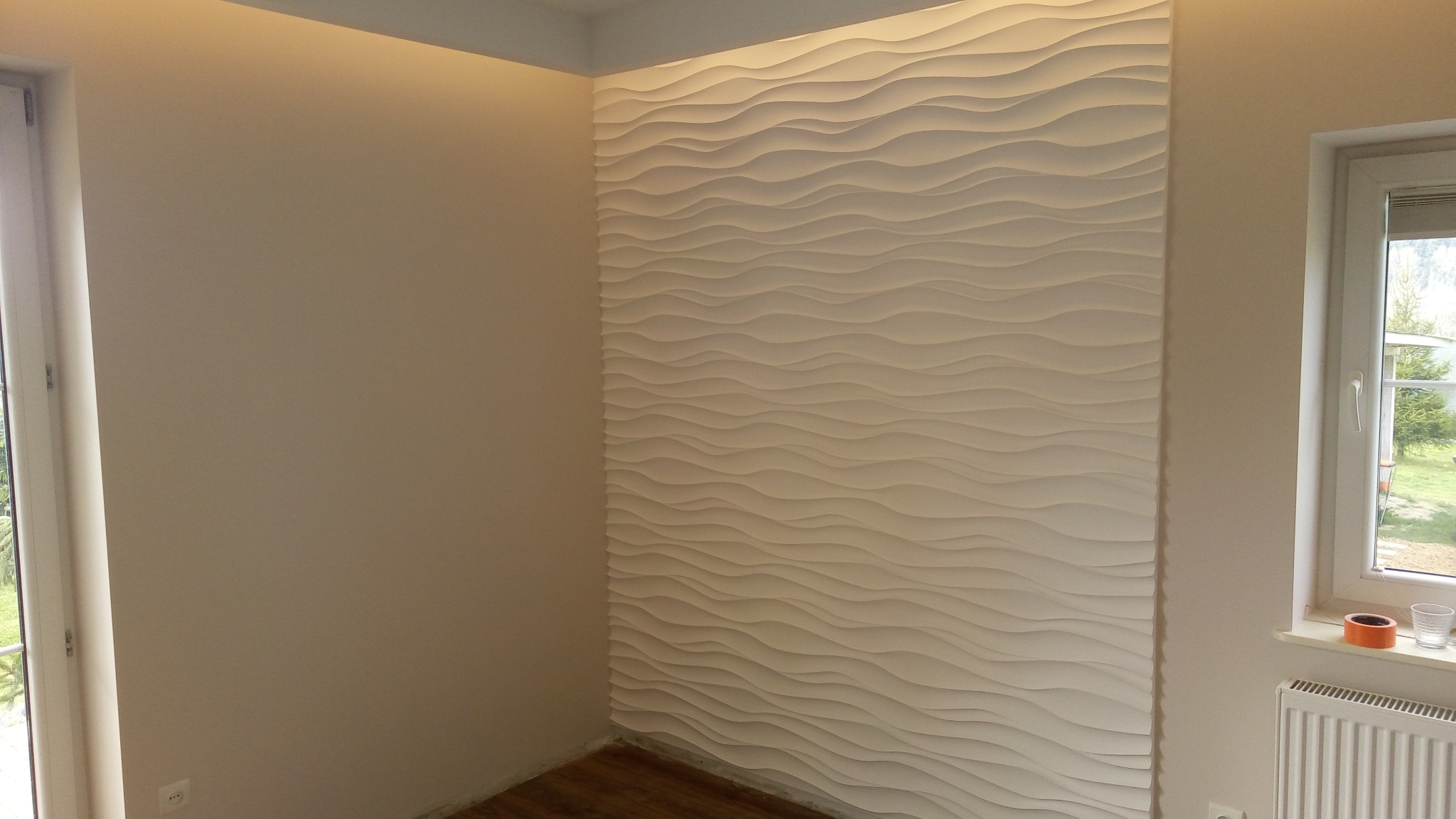 Pokój z dekoracyjną ścianą o falującej strukturze, podświetlona listwą LED, widok na okno z parapetem i grzejnikiem.