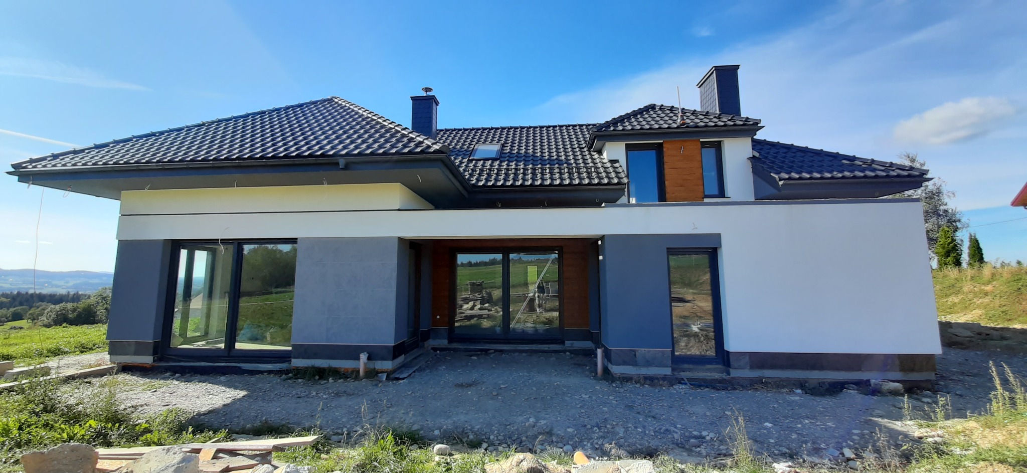 Nowoczesny dom jednorodzinny z ciemną dachówką i dużymi oknami w Gorlicach, widok z zewnątrz na tle wzgórz.