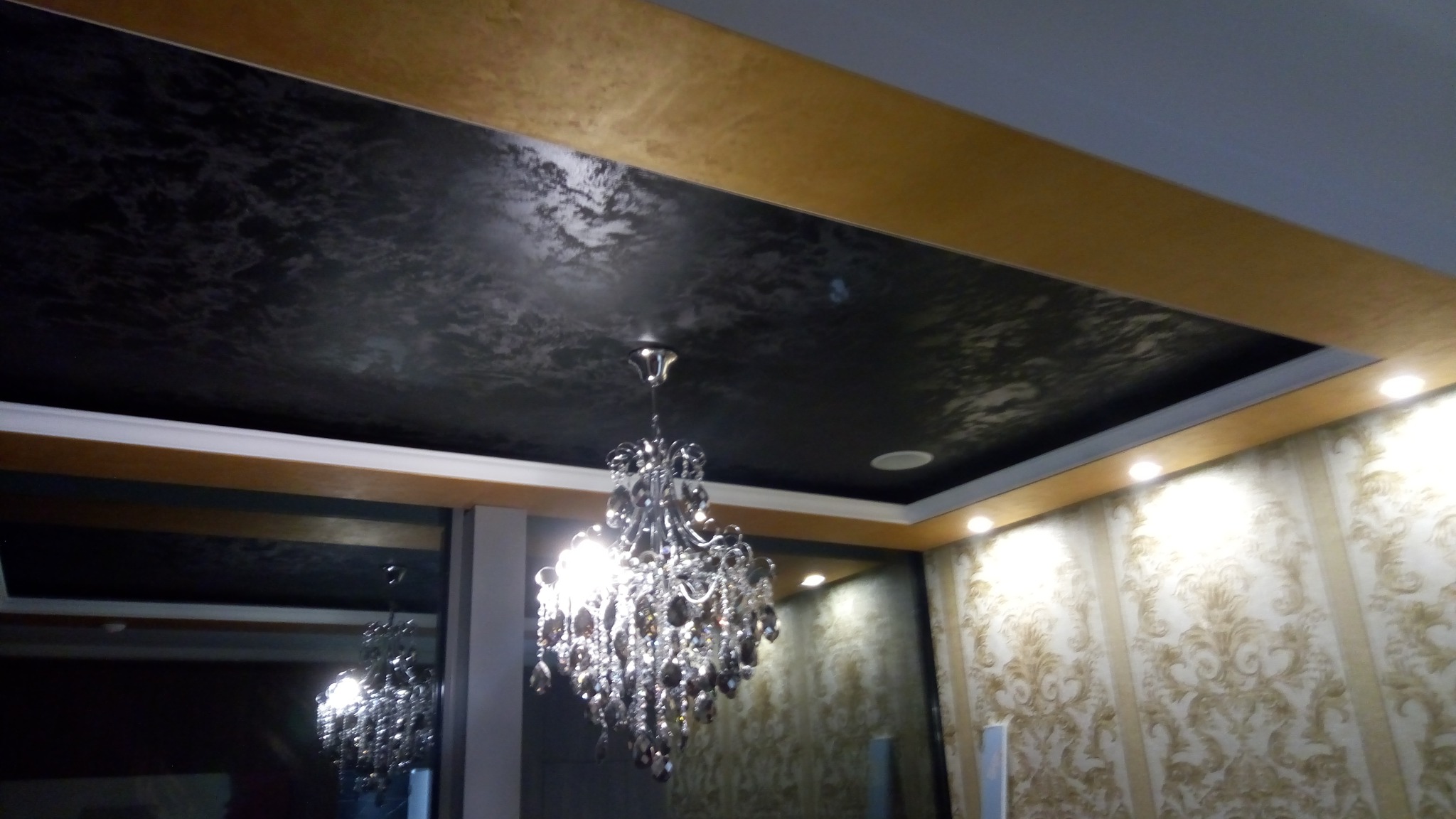 Elegancki salon z czarnym, teksturowanym sufitem, ozdobnym żyrandolem kryształowym i tapetą w złote wzory.