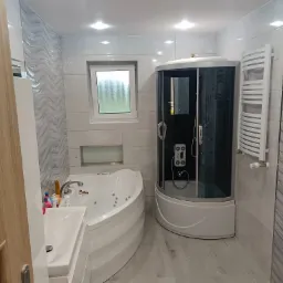 Nowoczesna łazienka w odcieniach szarości i bieli z kabiną prysznicową z hydromasażem, wanną z hydromasażem, grzejnikiem drabinkowym i dekoracyjnymi płytkami ściennymi z motywem fali.