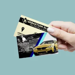 Dłoń trzymająca dwie wizytówki z projektami graficznymi dla firm z branży motoryzacyjnej z Wejherowa, prezentujące logo, dane kontaktowe i zdjęcia samochodów.