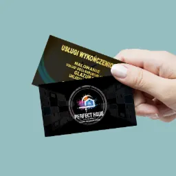 Dwie wizytówki firmy 'Perfect Haus' specjalizującej się w usługach wykończeniowych, trzymane w dłoni na jednolitym tle. Na jednej wizytówce wypisane usługi: malowanie, usługi ogólnobudowlane...
