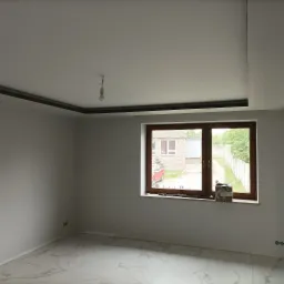 Wnętrze po remoncie: białe ściany, marmurowe płytki podłogowe, drewniane okno z widokiem na zewnątrz. Sufit z elementami dekoracyjnymi.