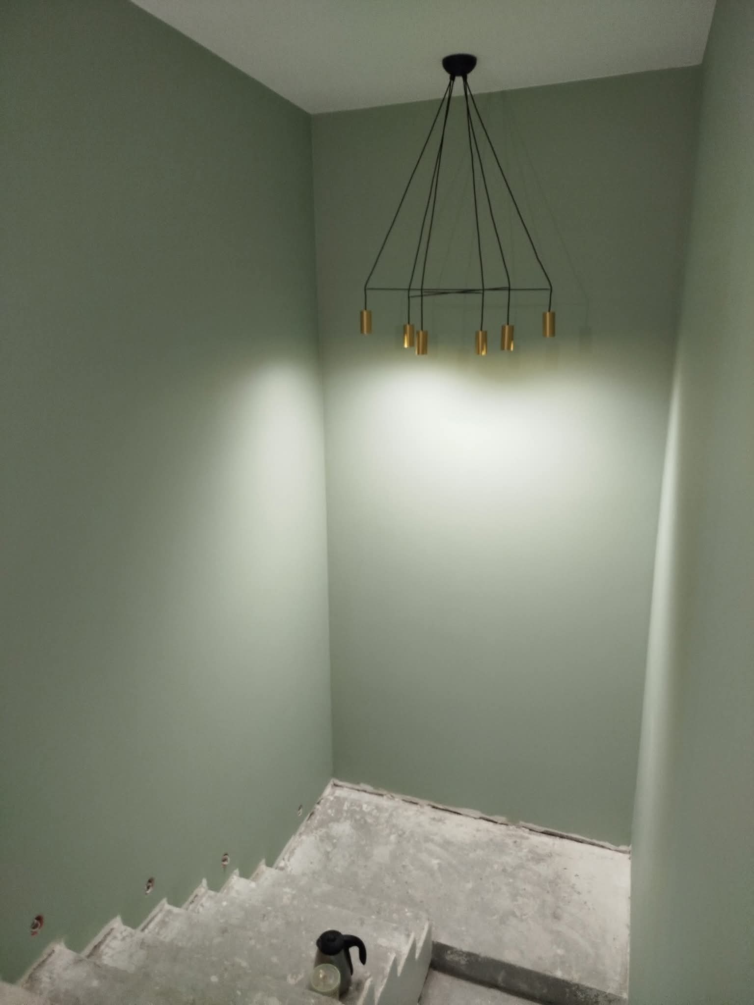 Świeżo pomalowane na oliwkowo schody z nowoczesną lampą wiszącą. Widoczne ślady po wcześniejszych pracach remontowych na stopniach.