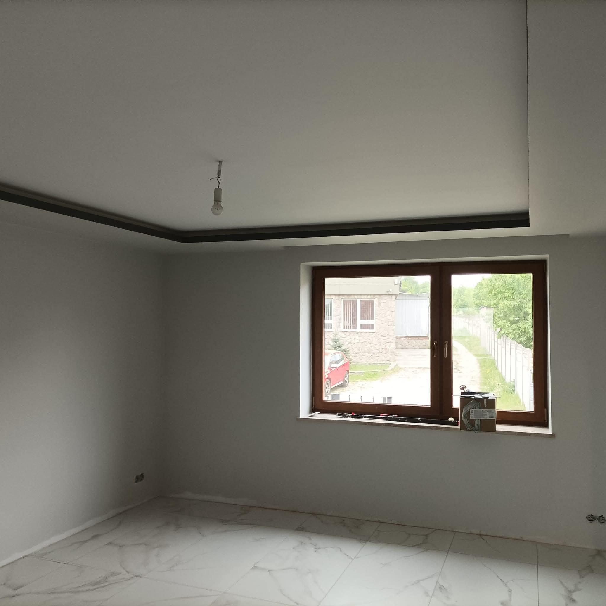 Wnętrze po remoncie: białe ściany, marmurowe płytki podłogowe, drewniane okno z widokiem na zewnątrz. Sufit z elementami dekoracyjnymi.