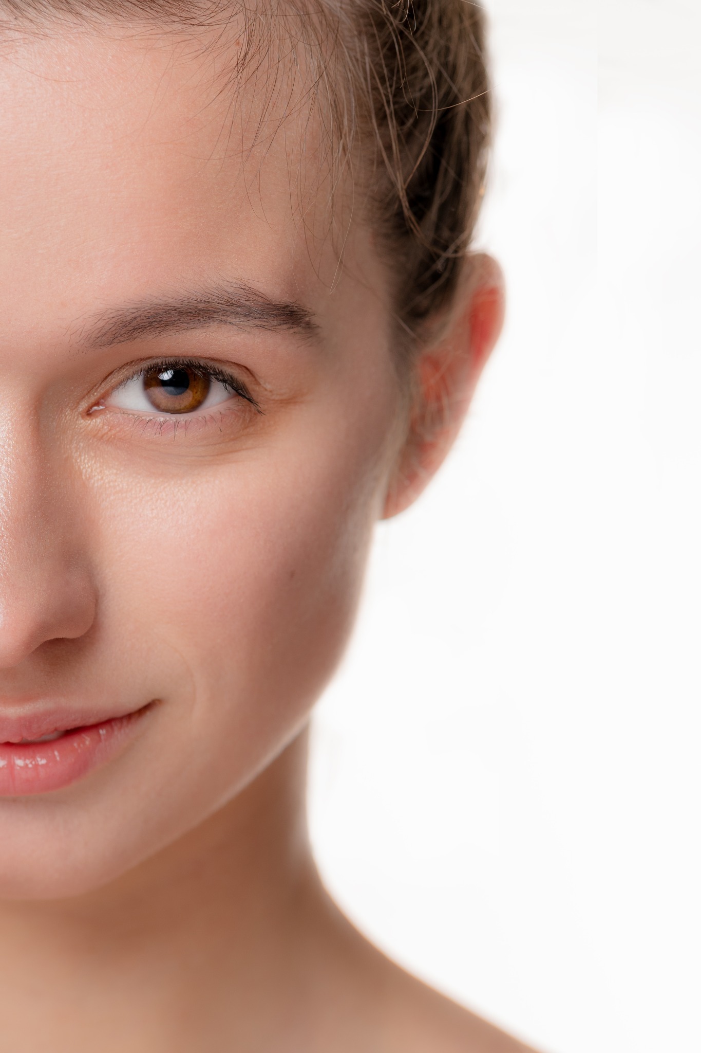 Portret zbliżeniowy połowy twarzy młodej kobiety z brązowymi oczami i delikatnym uśmiechem na jasnym tle.