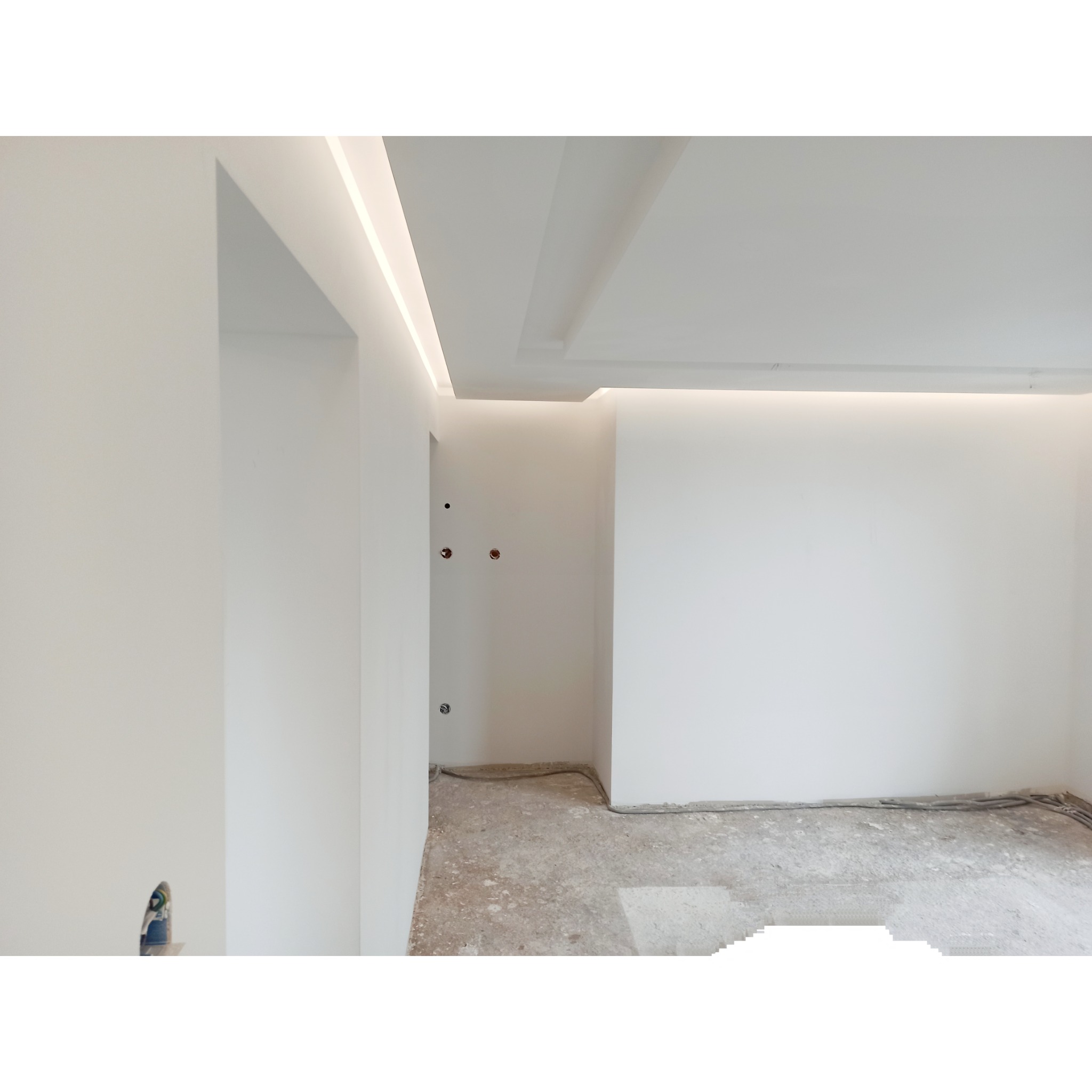 Wnętrze w trakcie prac wykończeniowych: białe ściany, surowa podłoga, widoczne instalacje elektryczne, oświetlenie LED w suficie.