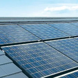 Niebieskie panele słoneczne zamontowane na szarym dachu z dachówki ceramicznej, widok z dołu pod kątem, błękitne niebo w tle.