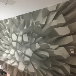 Fototapeta 3D z efektem geometrycznym w odcieniach szarości, imitująca rozkwitający kryształ, z widocznym panelem sterowania i gniazdkiem elektrycznym na ścianie.