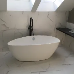 Nowoczesna, wolnostojąca wanna owalna z czarną armaturą na tle marmurowych płytek w łazience z oknem dachowym.