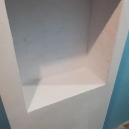 Wnęka ścienna z teksturą, pomalowana na biało, z widocznym fragmentem niebieskiej ściany w tle i drewnianej podłogi.