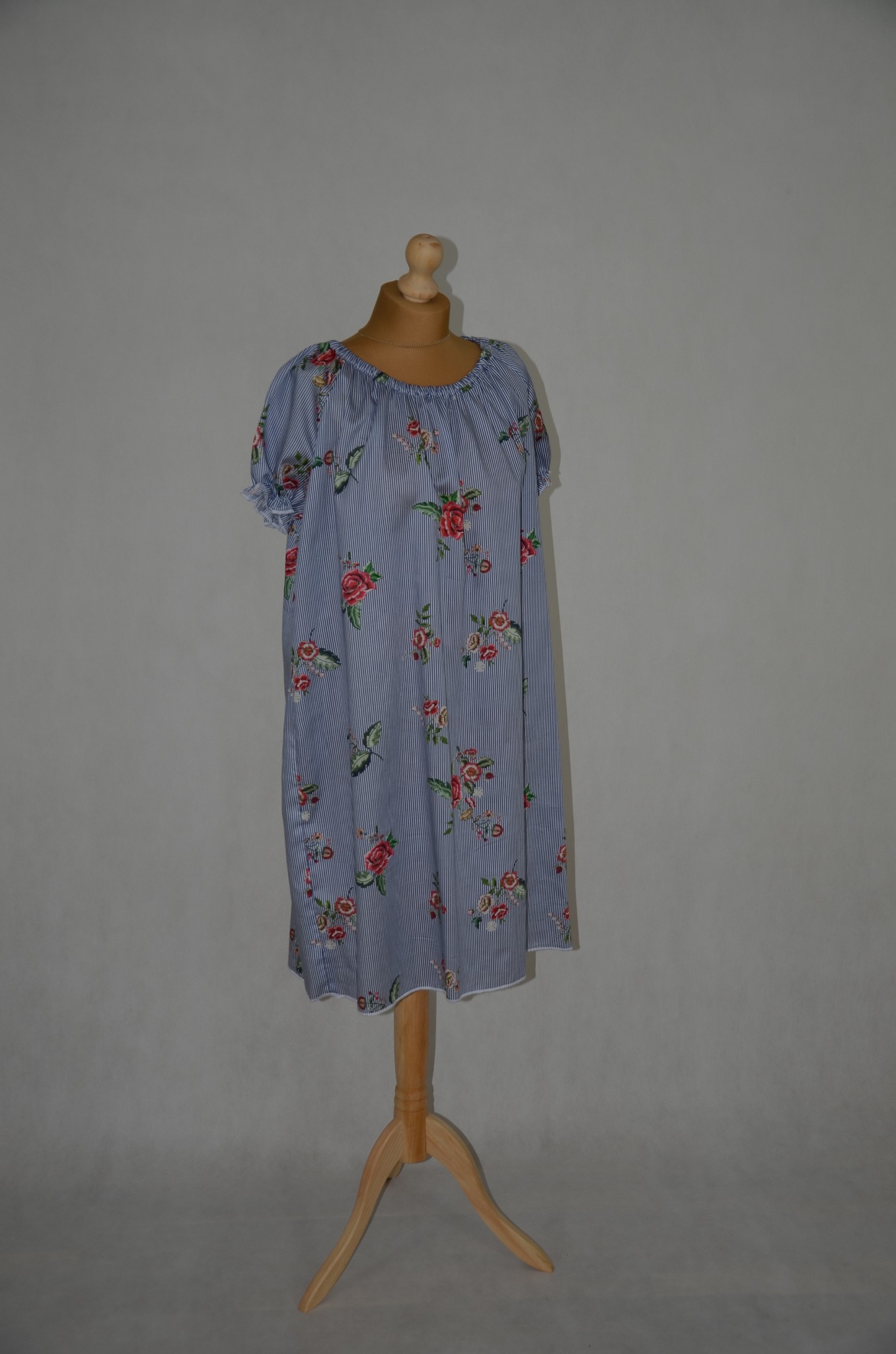 Letnia sukienka w paski z motywem róż, zaprezentowana na drewnianym manekinie na tle szarej ściany.