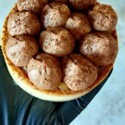 Widok z góry na okrągły deser z kremem czekoladowym posypanym kakao, leżący na czarnym podłożu.