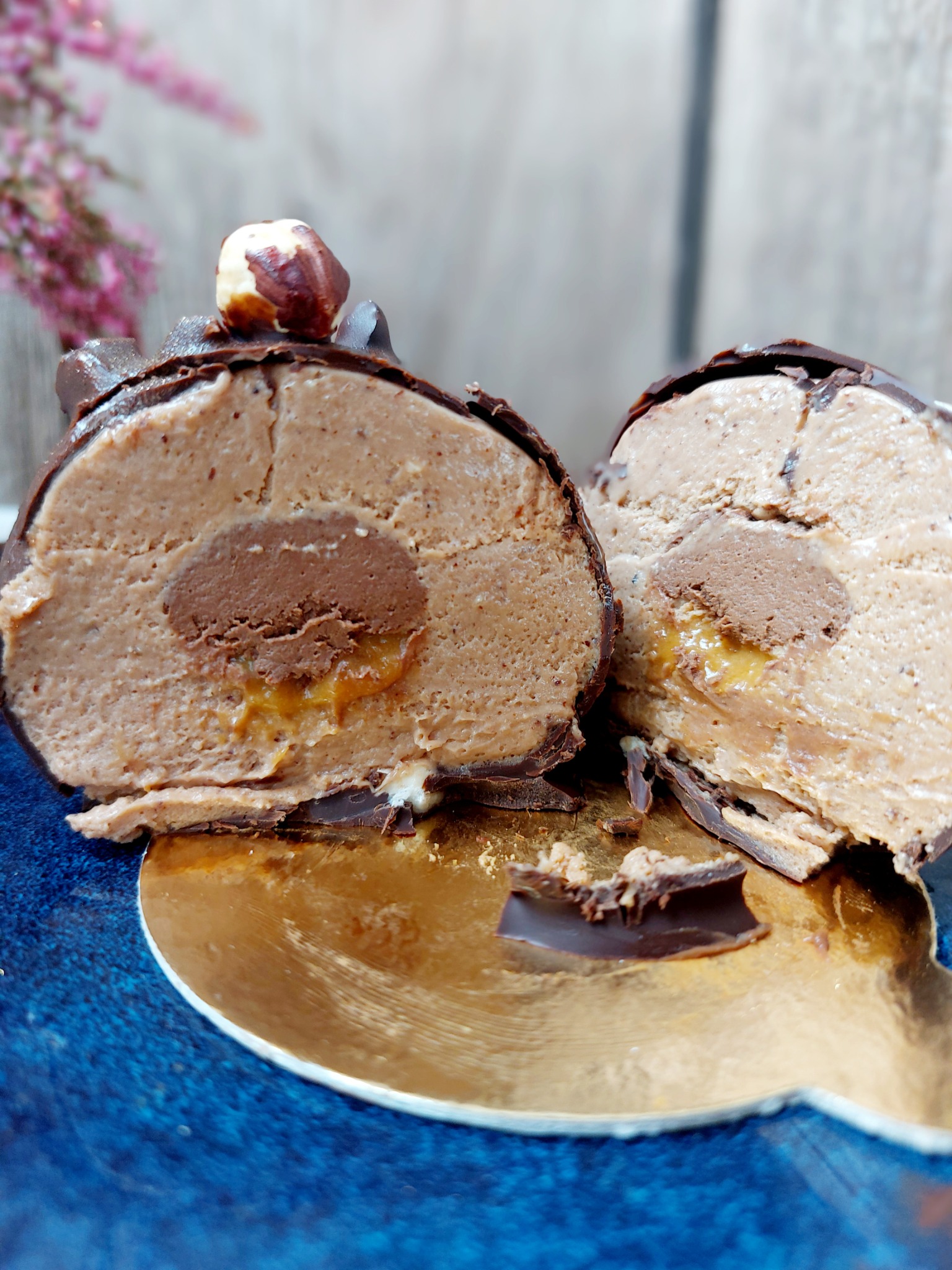 Przekrojony deser czekoladowy z orzechem laskowym na wierzchu, ukazujący kremowe wnętrze z karmelem, na złotej podkładce.