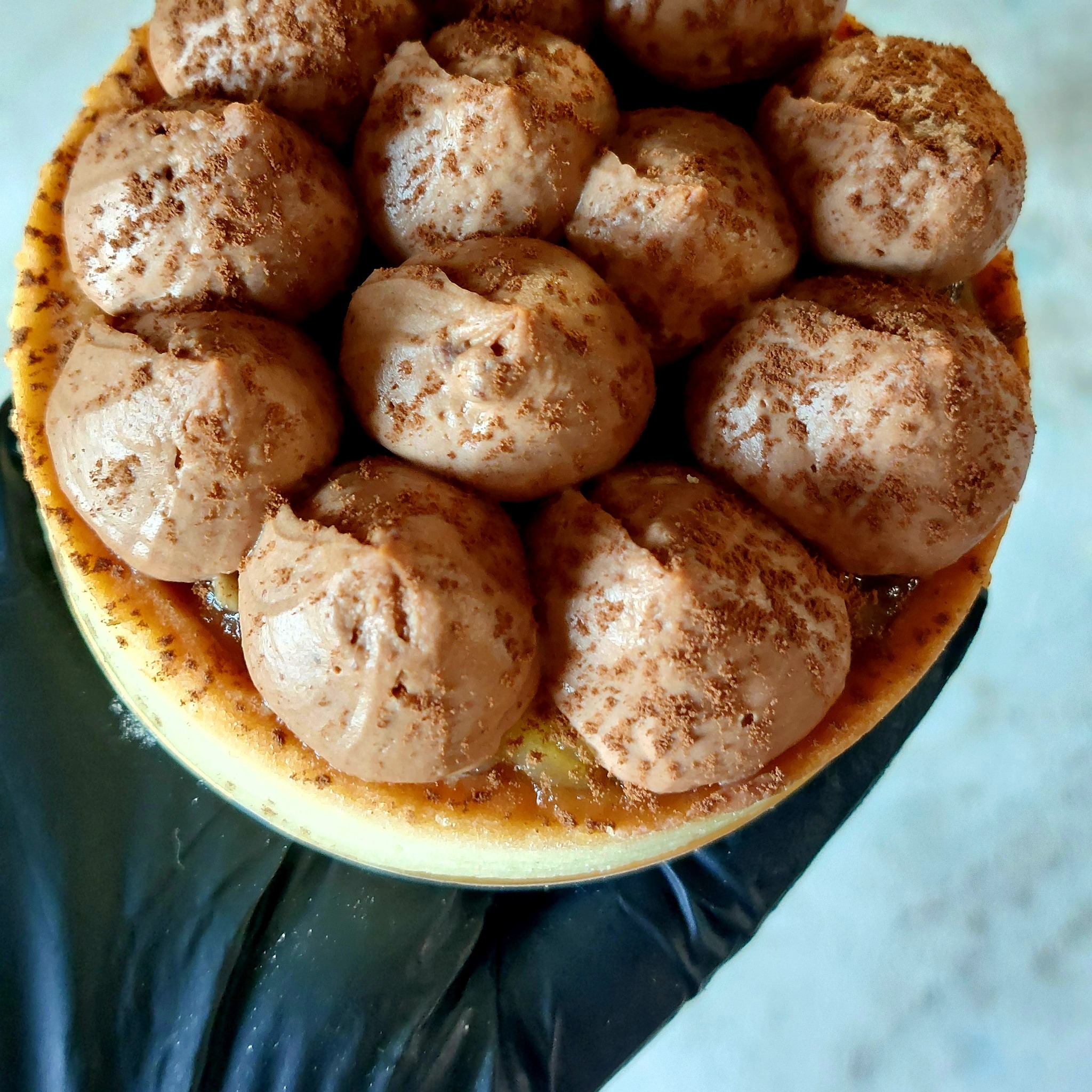 Widok z góry na okrągły deser z kremem czekoladowym posypanym kakao, leżący na czarnym podłożu.