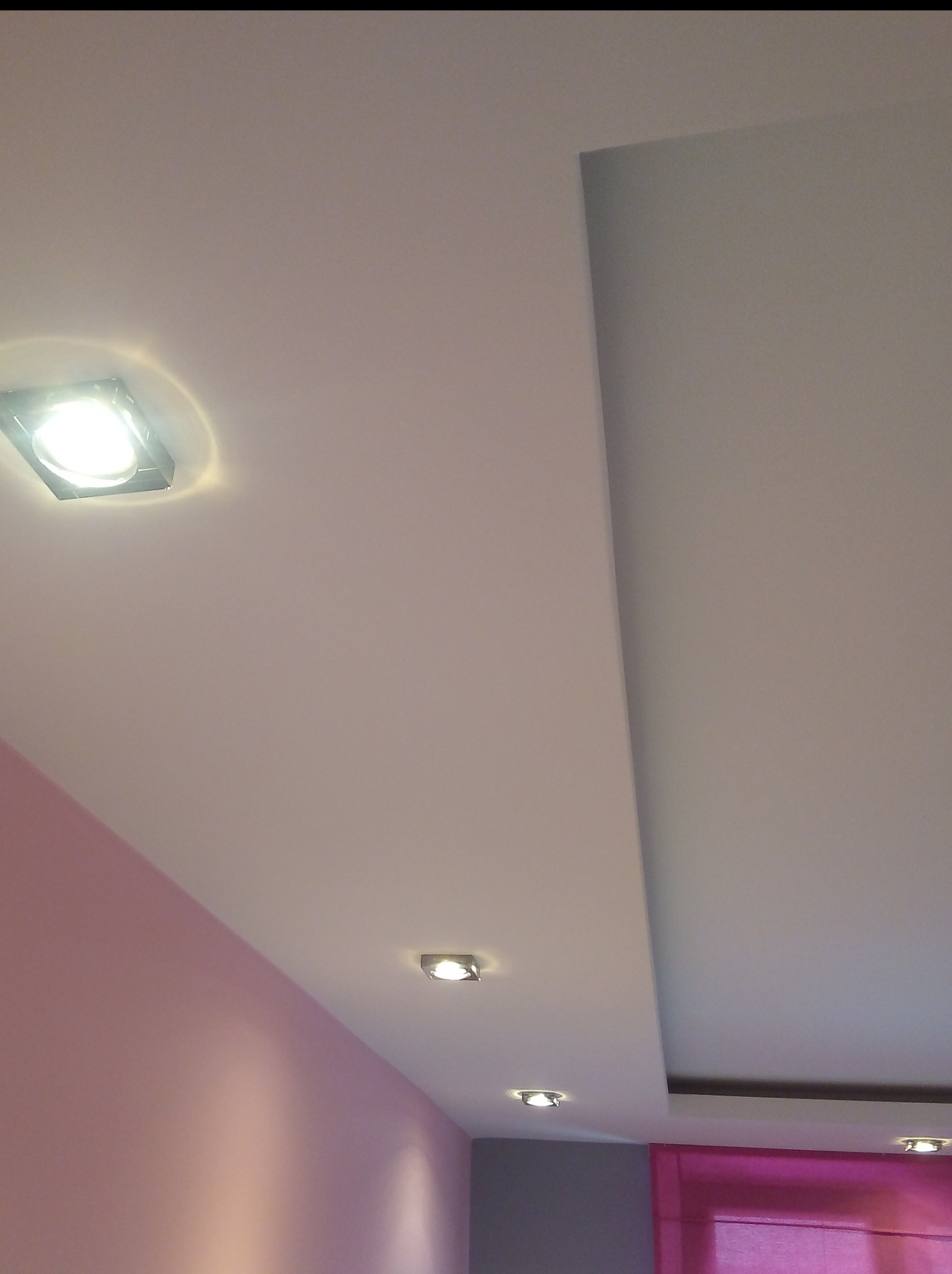 Wykończony sufit podwieszany z oświetleniem punktowym w Skarżysku-Kamiennej, fragment pomalowanej na różowo ściany w tle.