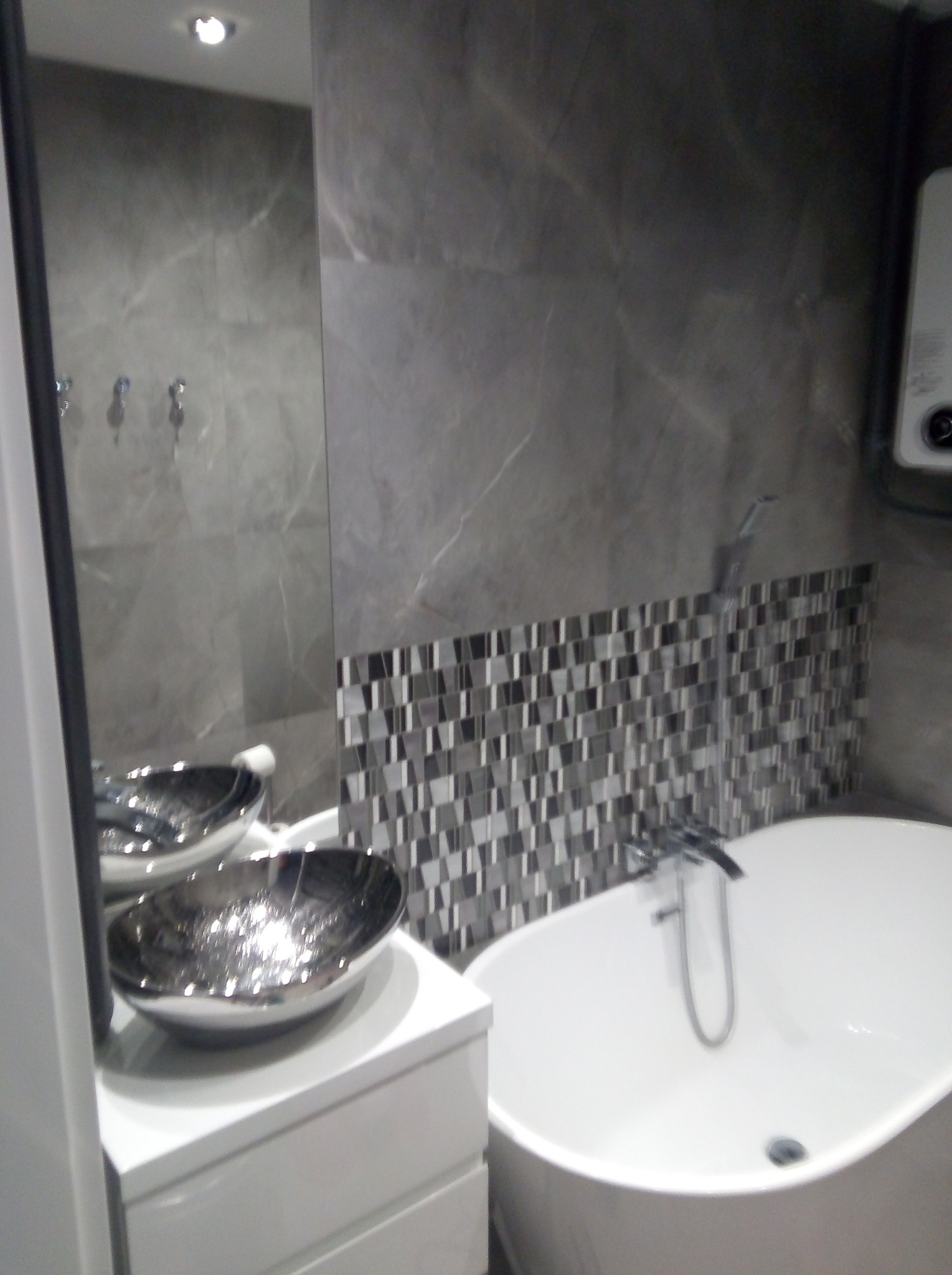 Nowoczesna łazienka z wolnostojącą wanną, umywalką w kształcie misy i szarą mozaiką na ścianie.