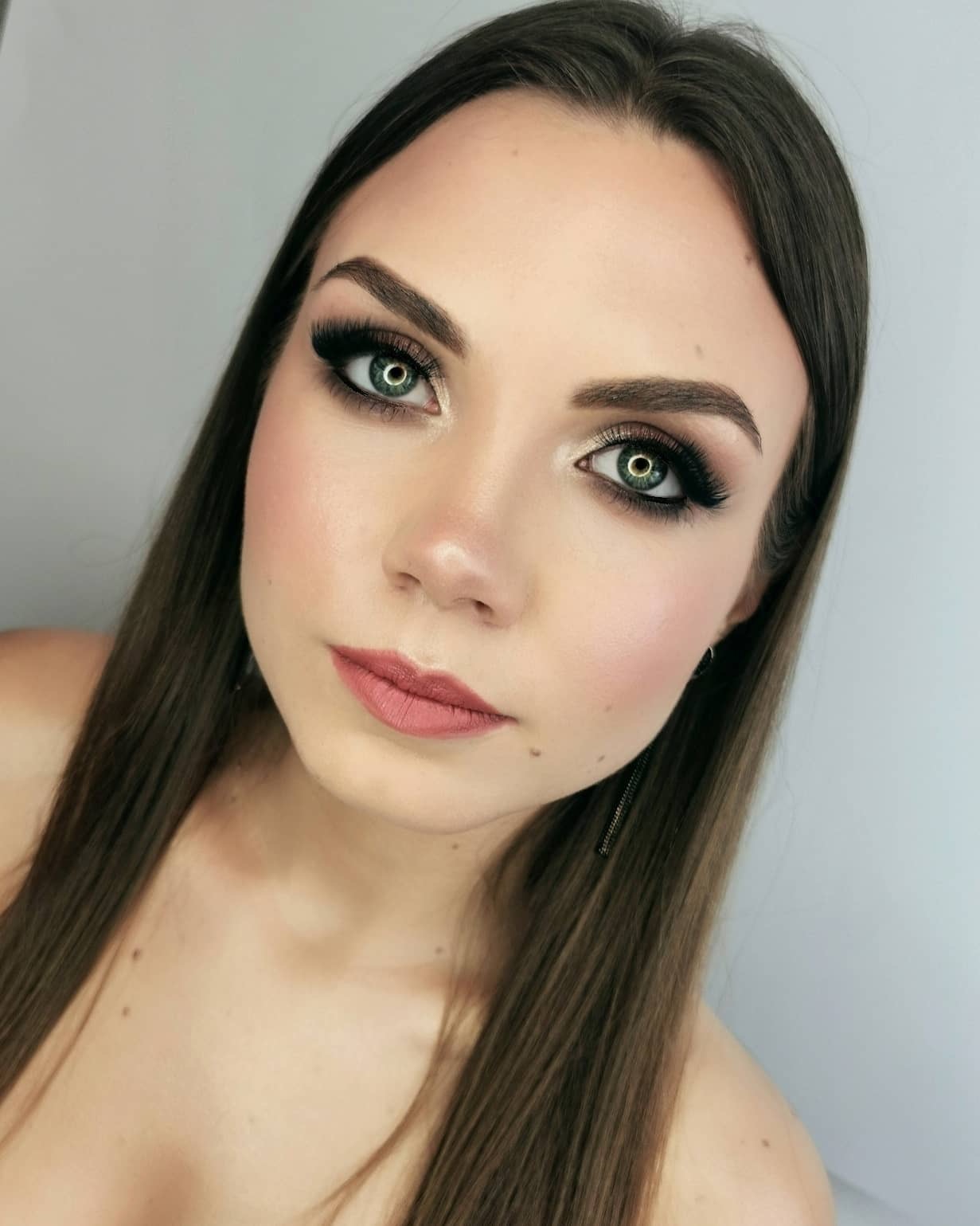 Portret kobiety z intensywnym makijażem oczu, długimi rzęsami i delikatnym różem na policzkach, prezentujący efekt końcowy zabiegu kosmetycznego.