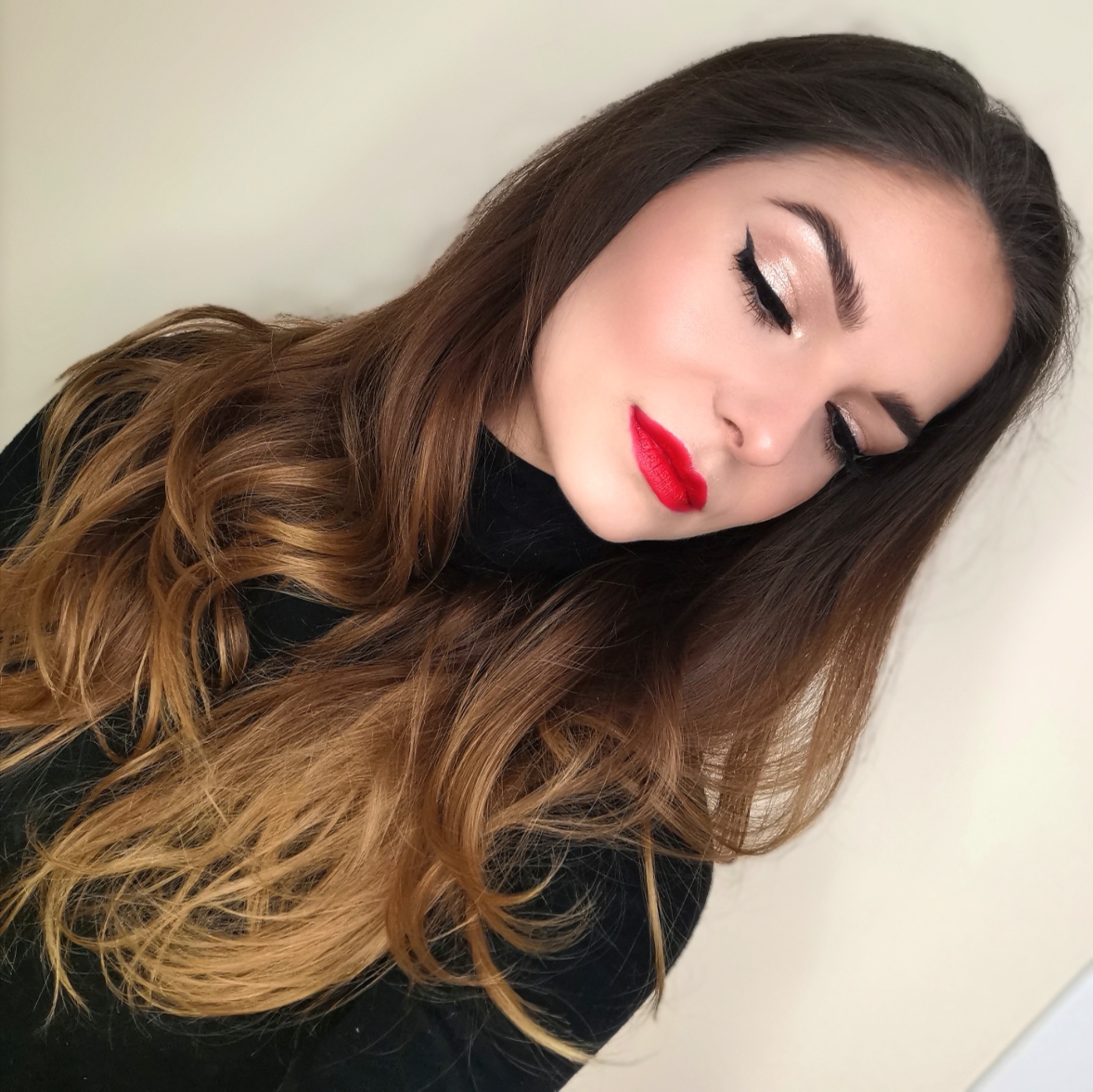 Portret kobiety z wyrazistym makijażem: czerwone usta, czarny eyeliner i błyszczący cień do powiek, brązowe włosy z ombre.