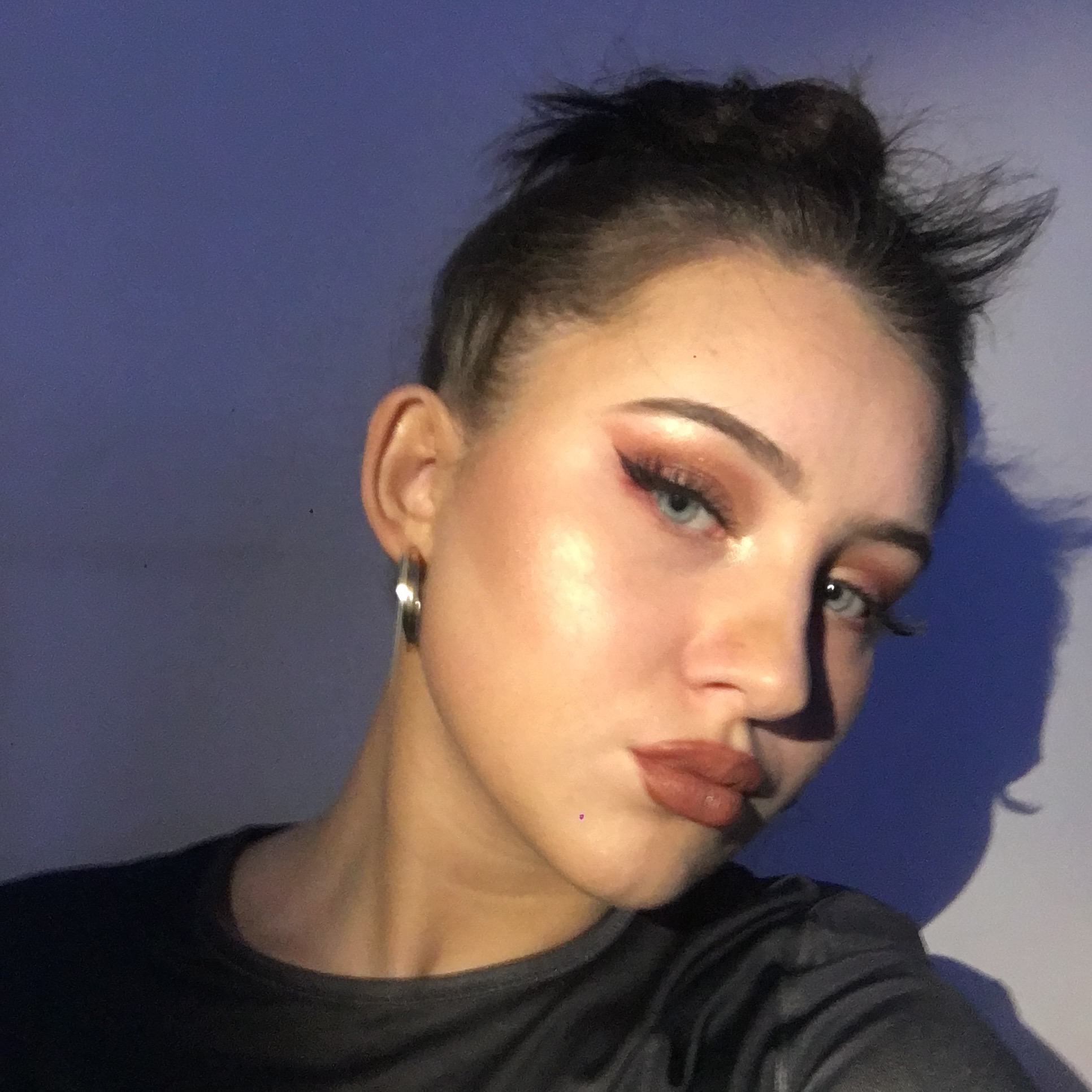 Portret kobiety z upiętymi włosami, widać makijaż oczu w odcieniach brązu i matową pomadkę na ustach, na uchu srebrny kolczyk koło