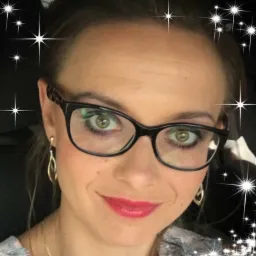 Portret kobiety w okularach z wzorzystymi zausznikami, z delikatnym uśmiechem, złotymi kolczykami i efektem rozbłysku gwiazd w tle.