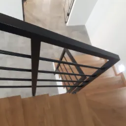 Nowoczesna balustrada ze stali nierdzewnej z czarnymi, geometrycznymi elementami na drewnianych schodach, widok z góry.