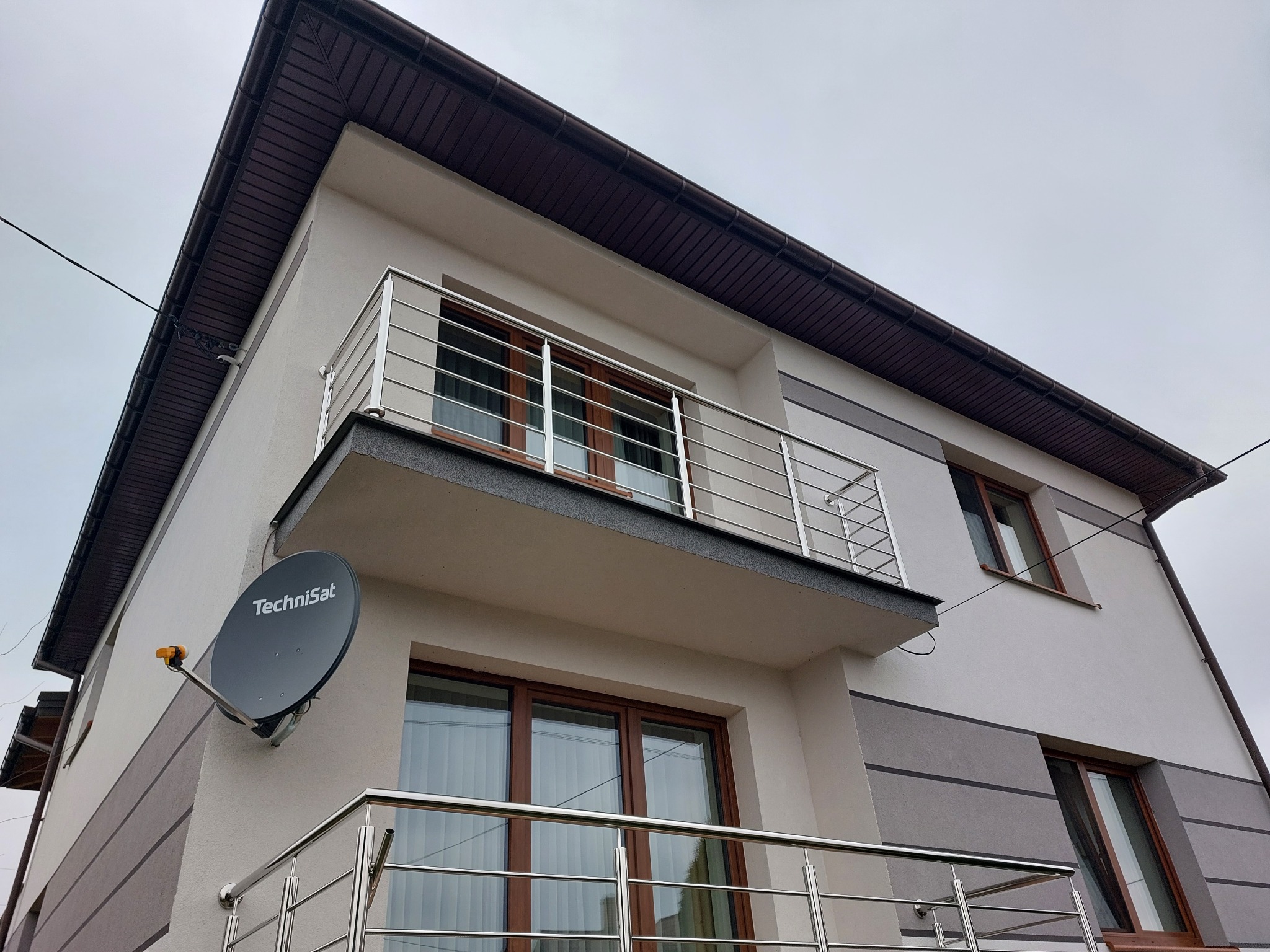 Nowoczesny dom z balkonami zabezpieczonymi metalowymi barierkami, na ścianie zamontowana antena satelitarna Technisat.