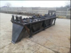 Czarna, metalowa konstrukcja spawana, prawdopodobnie element maszyny przemysłowej, na zewnątrz, szary beton i płot w tle.