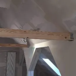 Poddasze w trakcie prac wykończeniowych: widoczne płyty kartonowo-gipsowe, ocieplenie podłogi wełną mineralną, drewniane belki konstrukcyjne i fragment grzejnika.