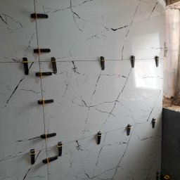 USŁUGI REMONTOWO BUDOWLANE KAROL GRABAREK - Ściana wyłożona białymi płytkami z czarnym wzorem żyłkowania, z użyciem klipsów poziomujących, w trakcie prac wykończeniowych w łazience.