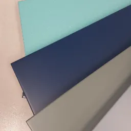 Próbki kolorów i materiałów wykończeniowych: ciemnoszary, turkusowy, granatowy, szary i biały, ułożone warstwami na jasnym blacie.