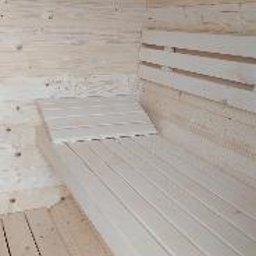 ABELIX Kamil Pawluk - Wnętrze sauny wykończone jasnym, surowym drewnem, ukazujące ławy i podłogę z desek, z widocznym zadaszeniem w kształcie łuku.