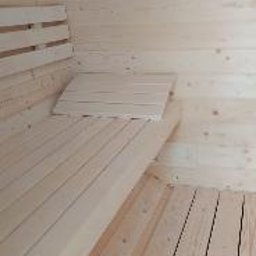 ABELIX Kamil Pawluk - Wnętrze sauny wyłożone jasnym drewnem, z ławkami i podkładką na siedzenie z tego samego materiału, widoczne sęki i naturalny rysunek drewna.