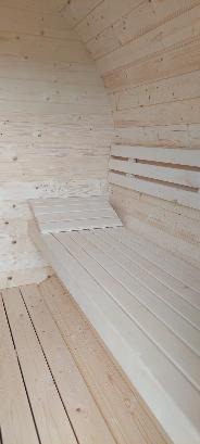 Wnętrze sauny wykończone jasnym, surowym drewnem, ukazujące ławy i podłogę z desek, z widocznym zadaszeniem w kształcie łuku.
