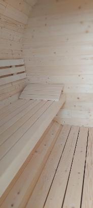 Wnętrze sauny wyłożone jasnym drewnem, z ławkami i podkładką na siedzenie z tego samego materiału, widoczne sęki i naturalny rysunek drewna.