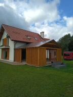 Jasny dom jednorodzinny z dobudowaną drewnianą werandą, widok z trawnika w pochmurny dzień.