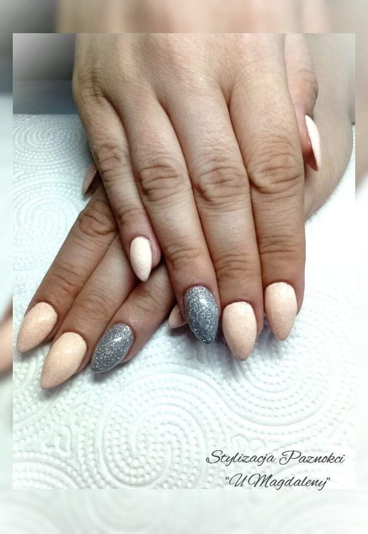 Dłonie z migdałowymi paznokciami, dwa pomalowane brokatowym, srebrnym lakierem, pozostałe w odcieniach beżu i różu na białym, teksturowanym tle.