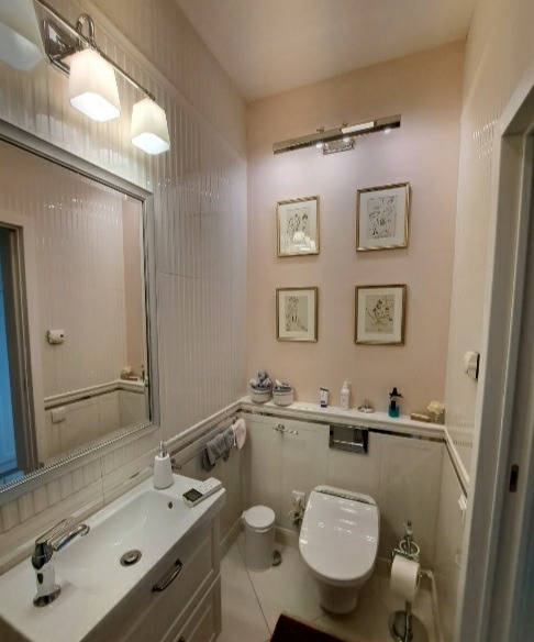 Jasna łazienka z toaletą myjącą, umywalką w zabudowie i czterema obrazkami w złotych ramach na ścianie w kolorze pudrowego różu.