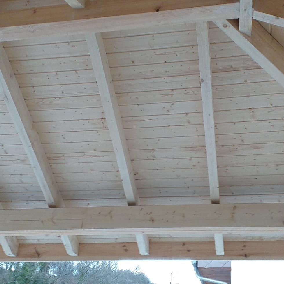Widok od spodu na nową drewnianą konstrukcję dachu z widocznymi belkami i deskami, surowe drewno, bez pokrycia dachowego.