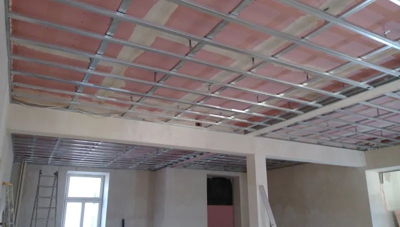 Widok sufitu w trakcie montażu stelaża z profili metalowych, przygotowanego pod płyty gipsowo-kartonowe, widoczna drabina oparta o ścianę przy oknie.