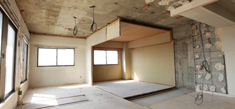 Wnętrze mieszkania w Domasławiu w trakcie remontu: odsłonięty betonowy sufit z wiszącymi kablami, fragmenty ścian bez tynku, widoczne okna.