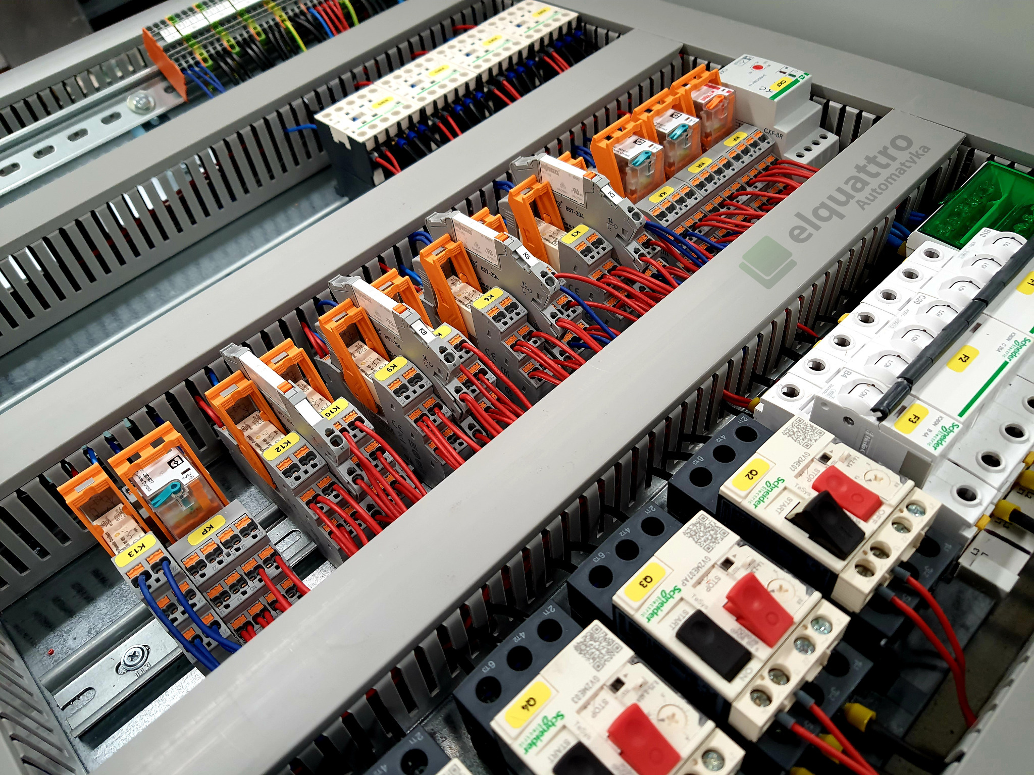 Wnętrze rozdzielnicy elektrycznej z modułami przekaźnikowymi, bezpiecznikami i okablowaniem, widoczne elementy Schneider Electric i Phoenix Contact, etykiety z oznaczeniami K1-K13 i Q2-Q4.