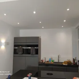 Szare szafki kuchenne z wbudowanymi piekarnikami i płytą indukcyjną, oświetlenie punktowe sufitowe, minimalistyczny design.