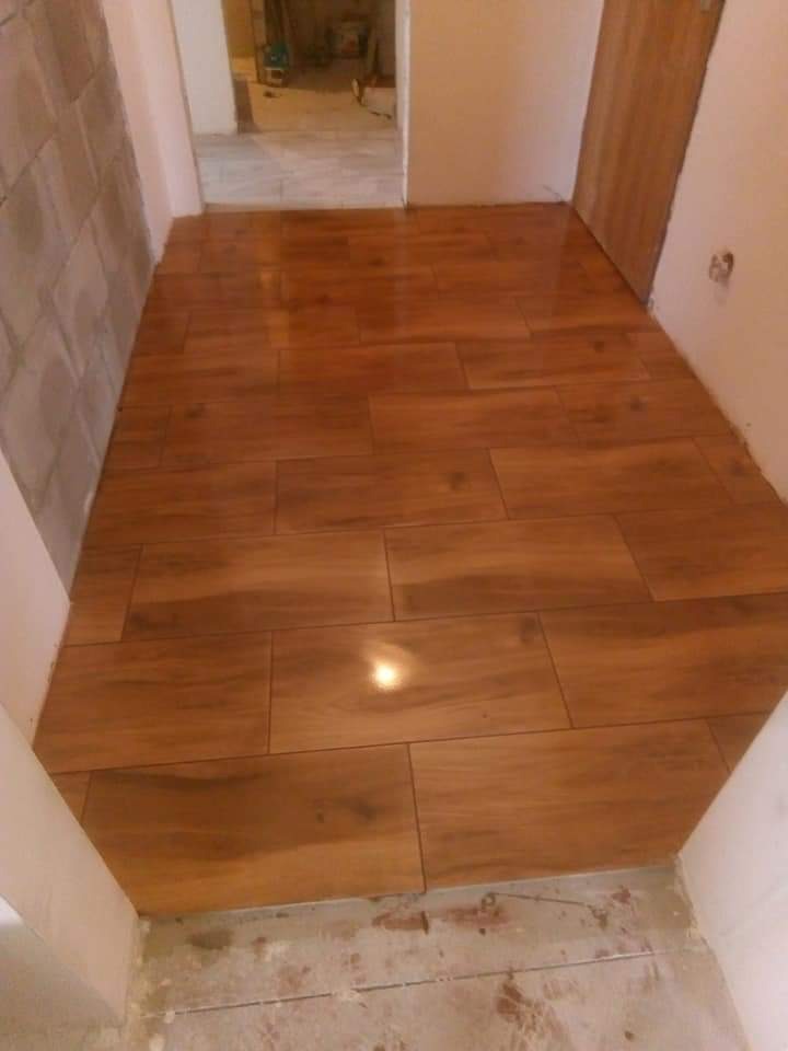 Ułożona, błyszcząca podłoga z płytek imitujących drewno w korytarzu w Oświęcimiu. Widoczne niedociągnięcia przy ścianach wymagające wykończenia.