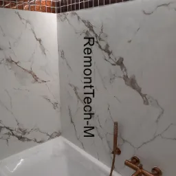 Biała wanna z marmurowymi płytkami i dekoracyjnym, brązowym pasem mozaiki pod sufitem, oświetlonym ledami. Bateria w kolorze miedzi dopełnia wystrój.